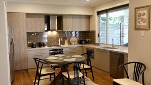 Een moderne keuken met een eethoek, met een ronde tafel en stoelen, een inbouwoven en een raam met zonwering.