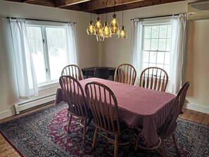 A dining area with a round table, six wooden chairs, a patterned rug, and a chandelier. - Cozy Vermont Lodge Near Jay Peak with Fire Pit (Troy)