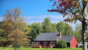 A red house with a porch and a chimney, surrounded by a green lawn and trees.