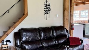 A wooden-framed room with a leather sofa, a small wooden table, and a wall-mounted tree decal.