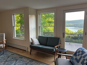 Relax in this inviting living room with a sofa, armchair, and small table, offering a serene view of the surrounding landscape and water.