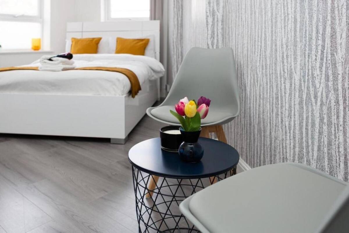 Een moderne hotelkamer met een net opgemaakt bed, een rond bijzettafeltje met een bloemenvaas en een grijze fauteuil.
