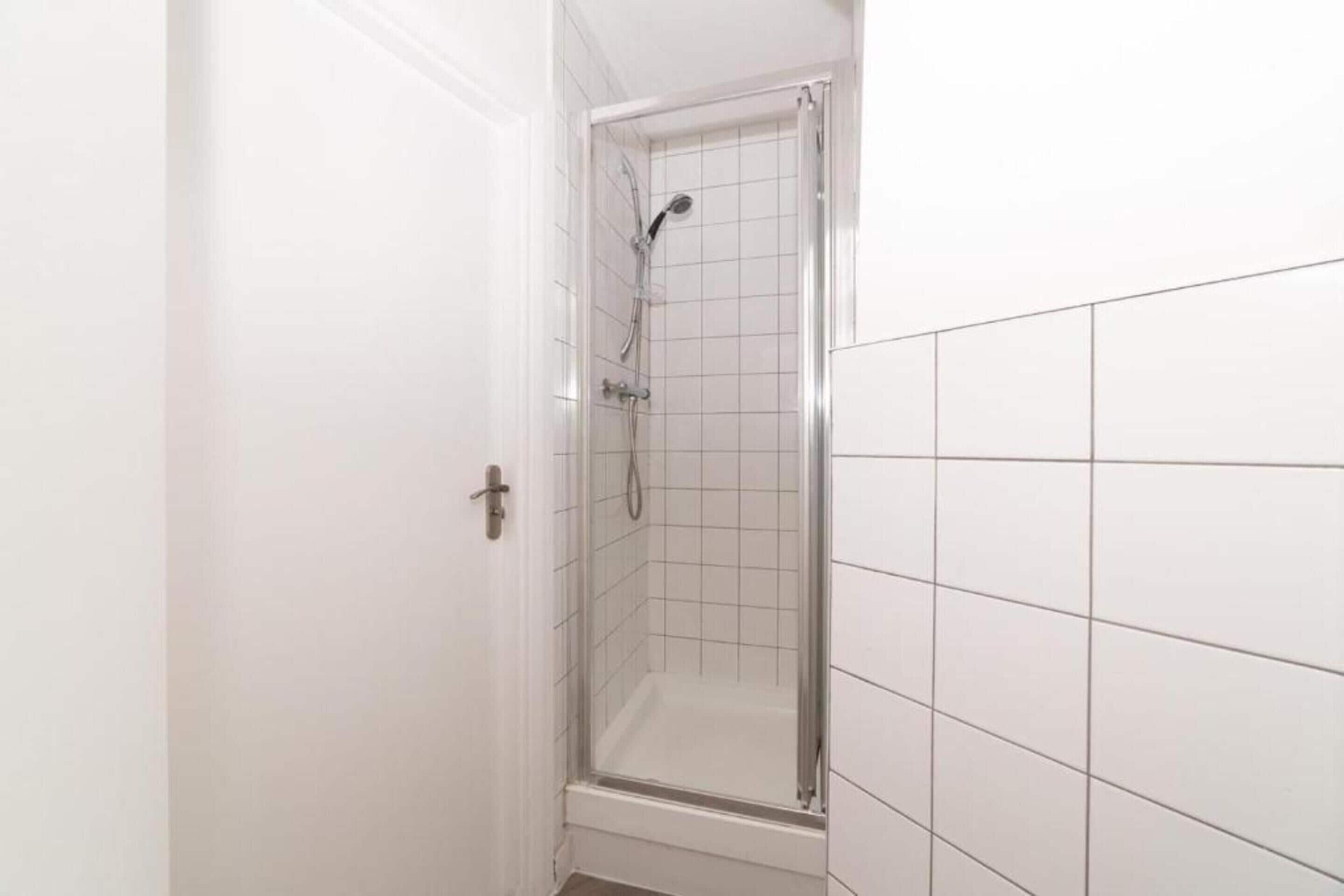 Ein Badezimmer mit einer gläsernen Duschkabine, weißen Fliesen und einer Tür mit silberner Griff.