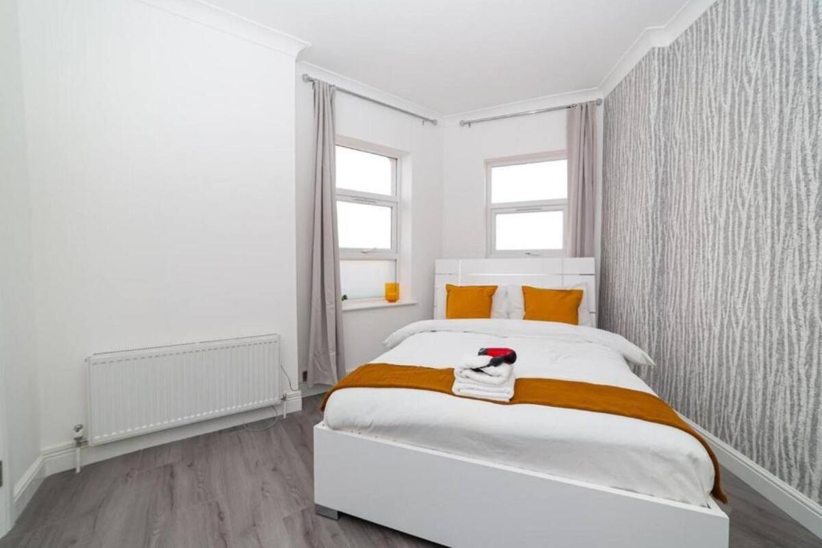 Een moderne slaapkamer met een wit bed, twee ramen, een radiator en een structuurwand.