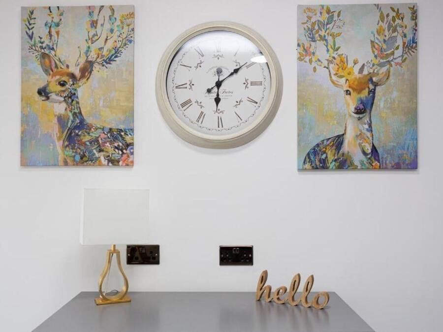 Un mur avec une horloge, deux tableaux représentant des cerfs, une lampe et une pancarte sur laquelle est écrit « Bonjour ».