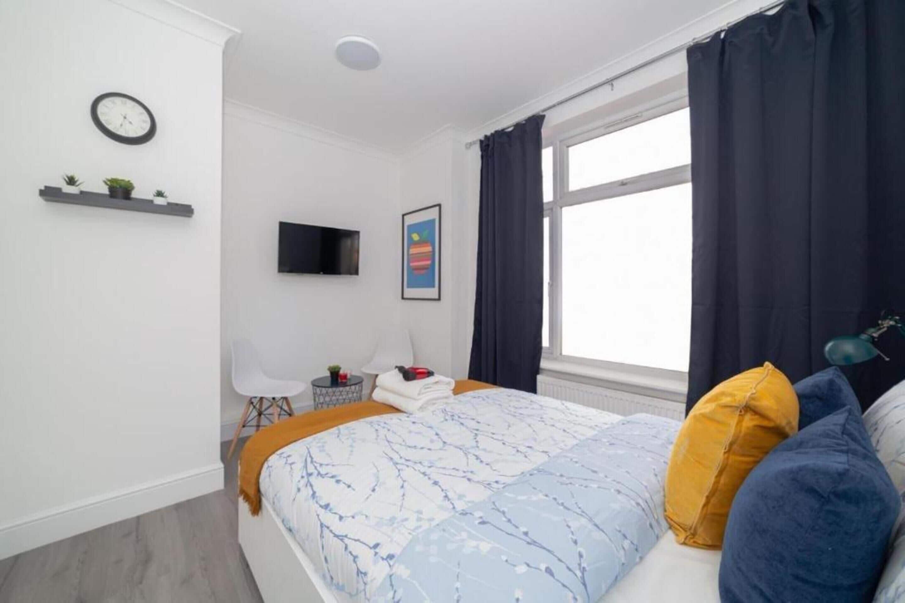 Une chambre moderne avec un lit, une télévision, un bureau et une fenêtre avec des rideaux.