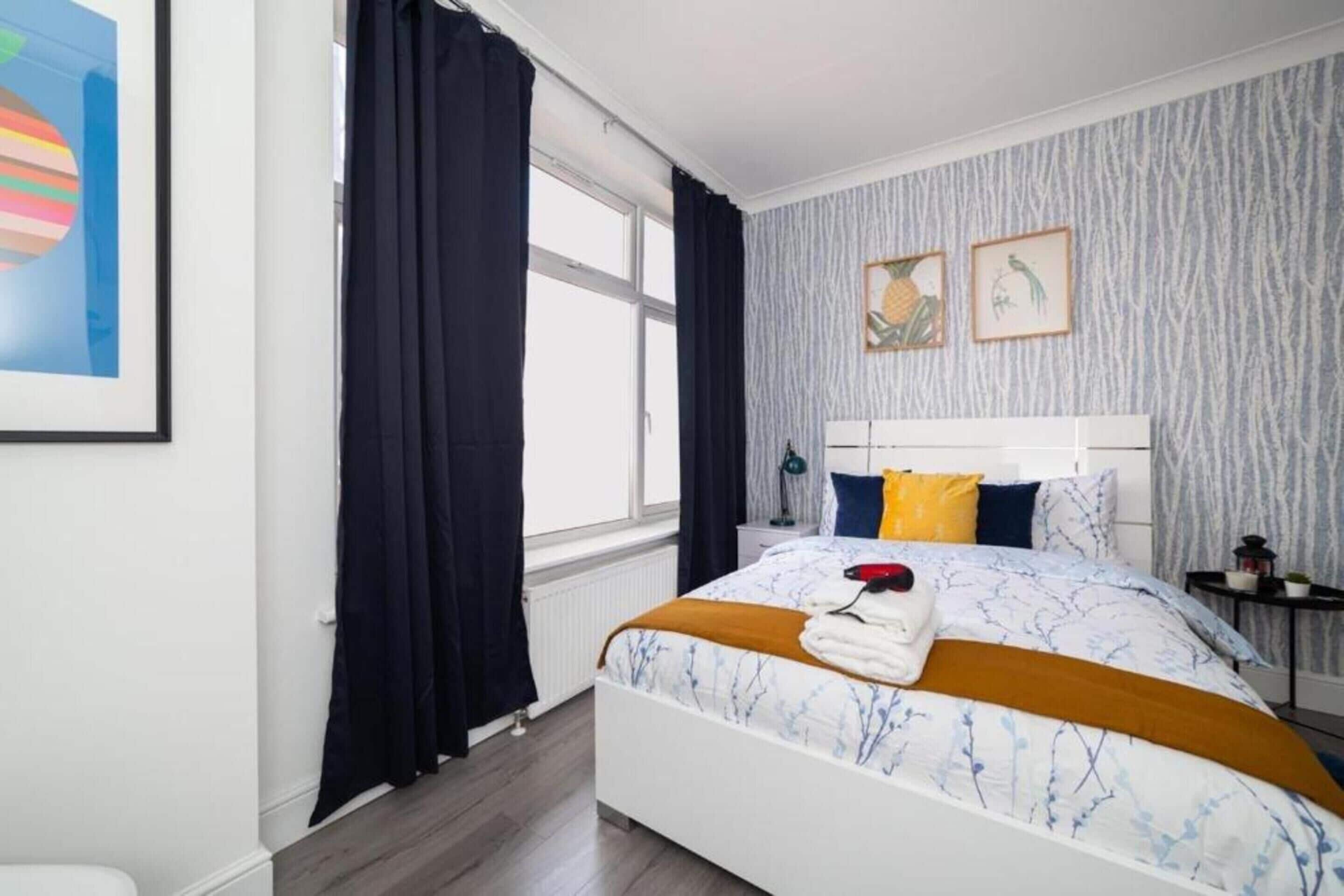 A bedroom with a bed, a window with curtains, a nightstand, and two framed pictures on the wall.