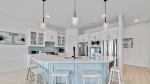 A modern kitchen with white cabinets, a central island with stools, stainless steel appliances, and pendant lighting. - PRIVATE LUXURY HOUSE, COMMUNITY POOL, WATERFRONT ON LITTLE LAGOON! (Gulf Shores)