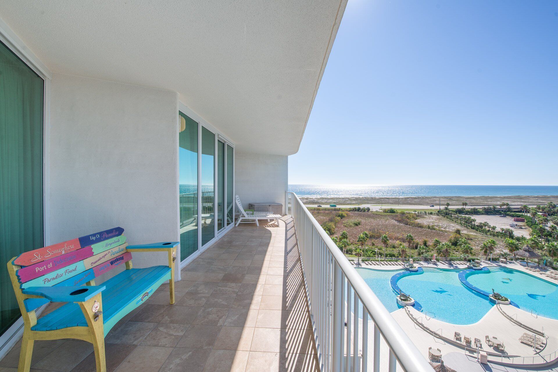 Een balkon met een bankje, een zwembad en uitzicht op het strand.