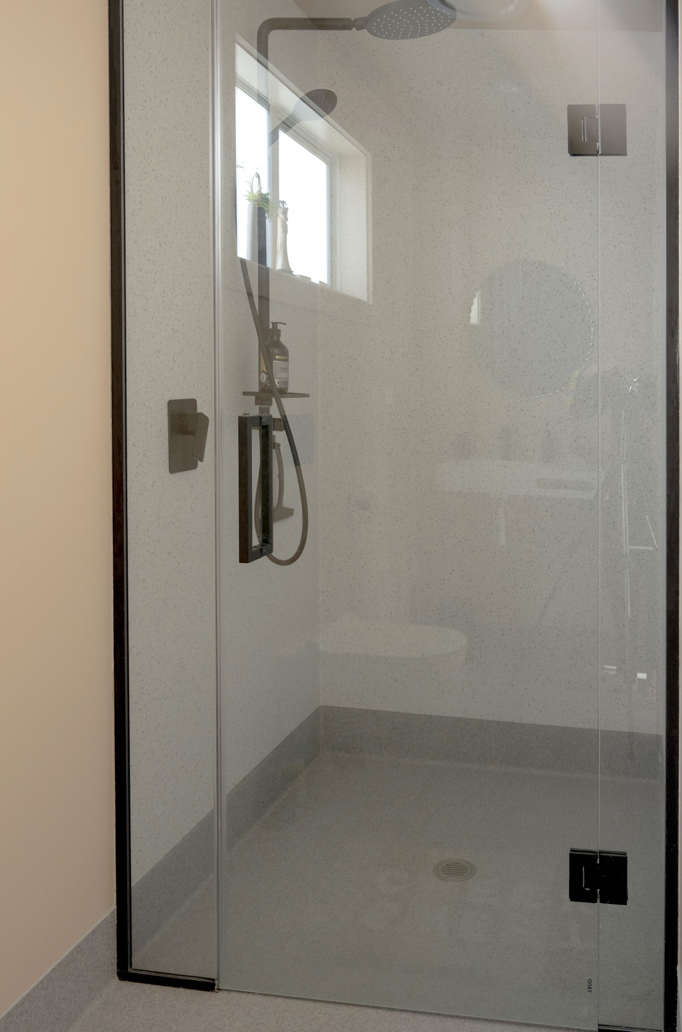 A glass-enclosed shower with a handheld showerhead and a wall-mounted control panel.