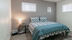A bedroom with a bed, bedside table, lamp, and a window.
