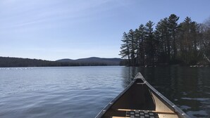 A canoe on calm water with a forested shoreline and distant hills. - Downtown Meredith Village Cape (Meredith)