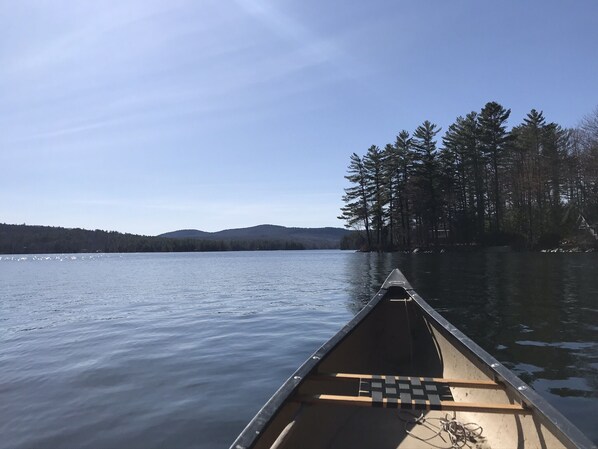 A canoe on calm water with a forested shoreline and distant hills.
