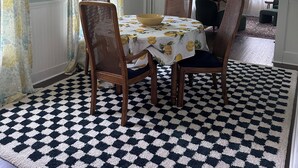 A dining area with a checkered rug, wooden chairs, and a table with a floral tablecloth. - Downtown Meredith Village Cape (Meredith)