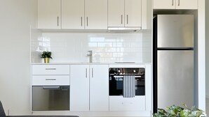 A modern kitchen with white cabinetry, a stainless steel refrigerator, and a built-in oven. - One on Harris Apartments (Wellington Point)