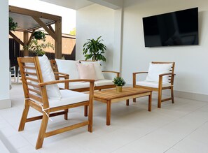 A modern outdoor seating area with wooden chairs and a table, surrounded by potted plants and a TV mounted on the wall. - One on Harris Apartments (Wellington Point)