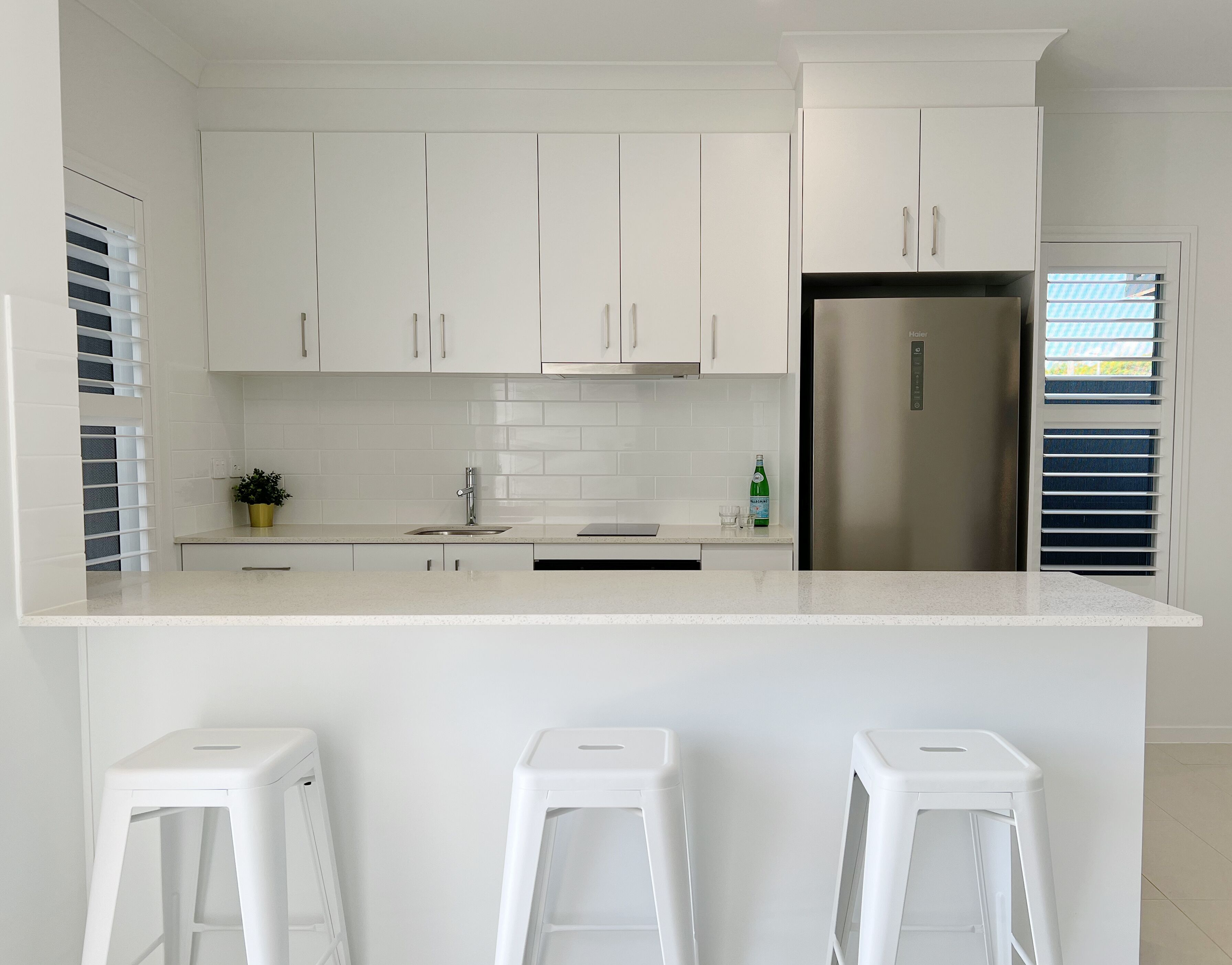 A modern kitchen with white cabinets, a stainless steel refrigerator, and a countertop with stools.