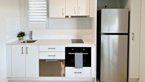 A modern kitchen with white cabinets, stainless steel appliances, and a window with blinds. - One on Harris Apartments (Wellington Point)