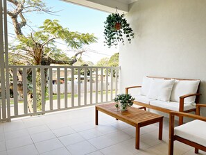 A balcony with a white railing, a wooden bench, a white sofa, and a hanging plant.