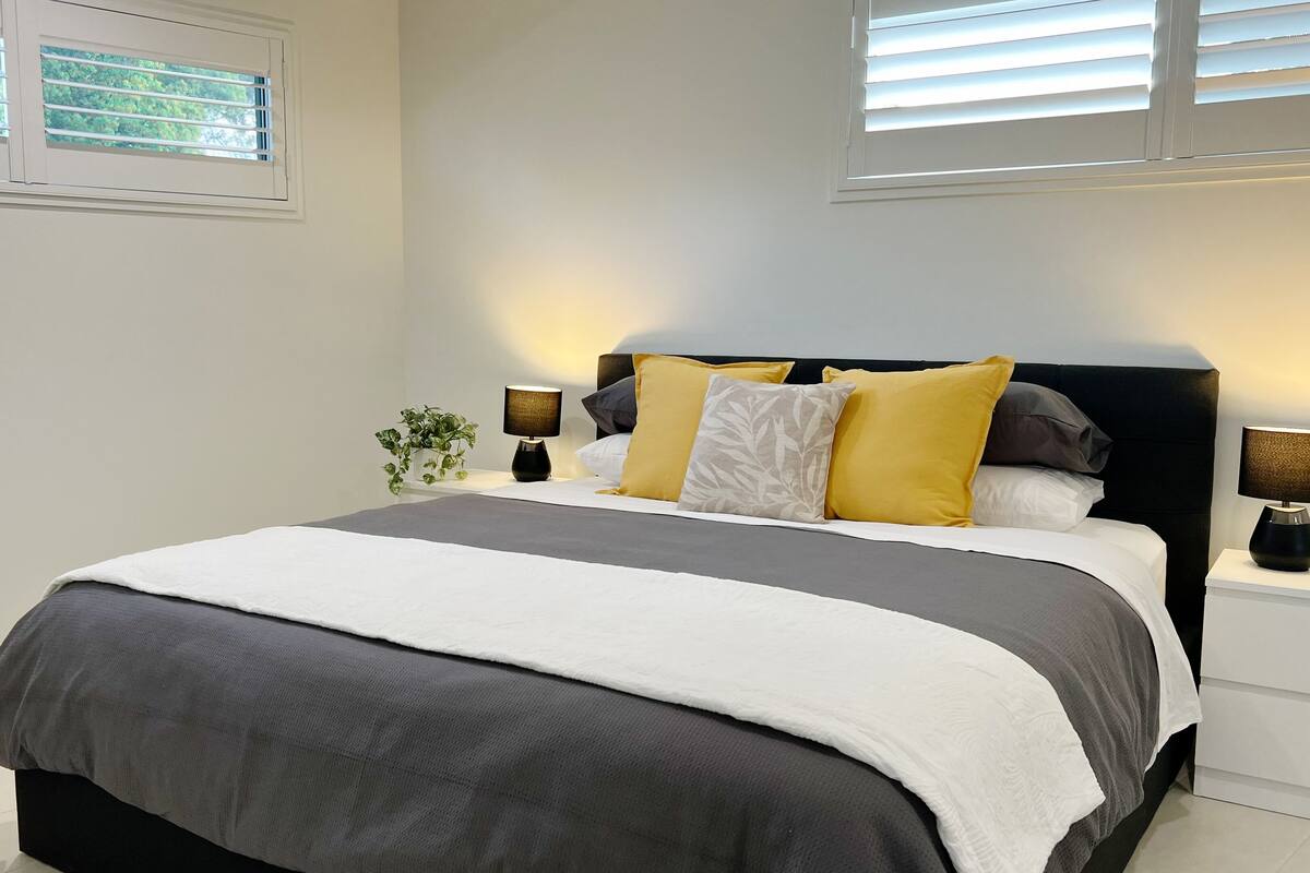 A bedroom with a bed, two bedside tables, a chair, and a window.