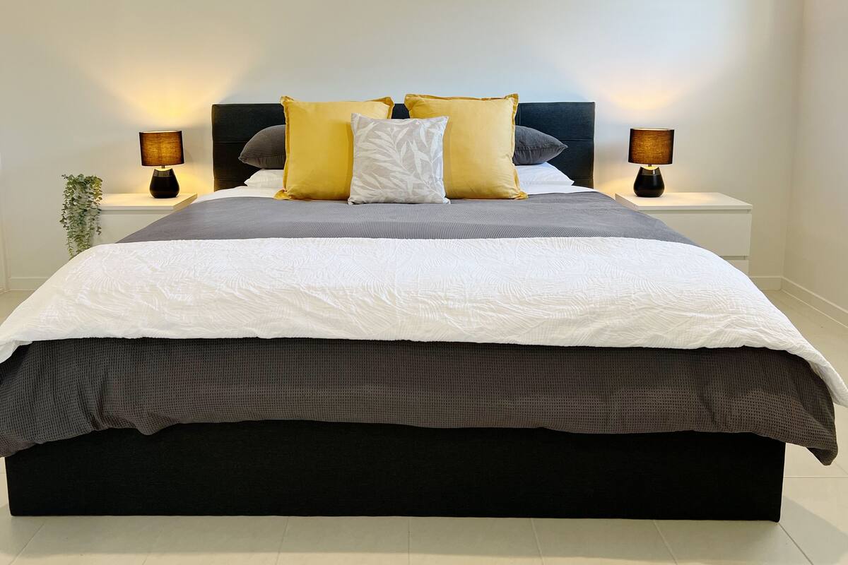 A modern bedroom with a large bed, two bedside tables, and a potted plant.