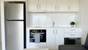 A modern kitchen with white cabinets, a stainless steel refrigerator, an oven, and a dishwasher. - One on Harris Apartments (Wellington Point)