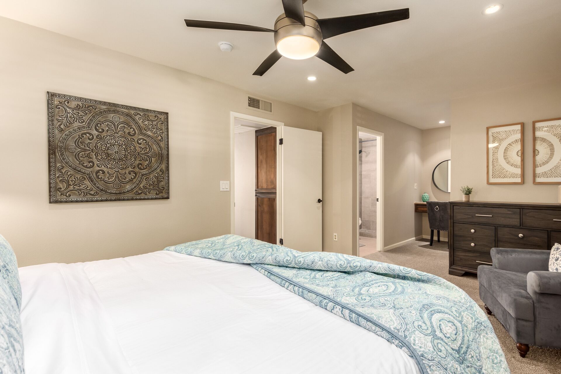 A bedroom with a bed, a dresser, a vanity, and a ceiling fan.