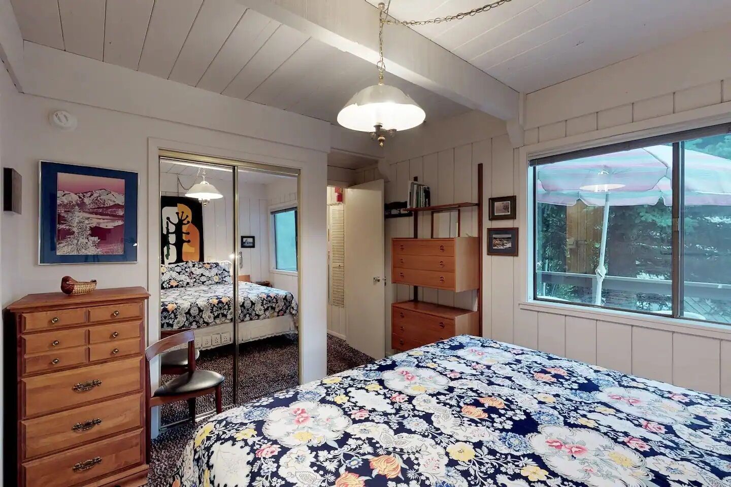 A bedroom with a bed, dresser, and a window with a view.