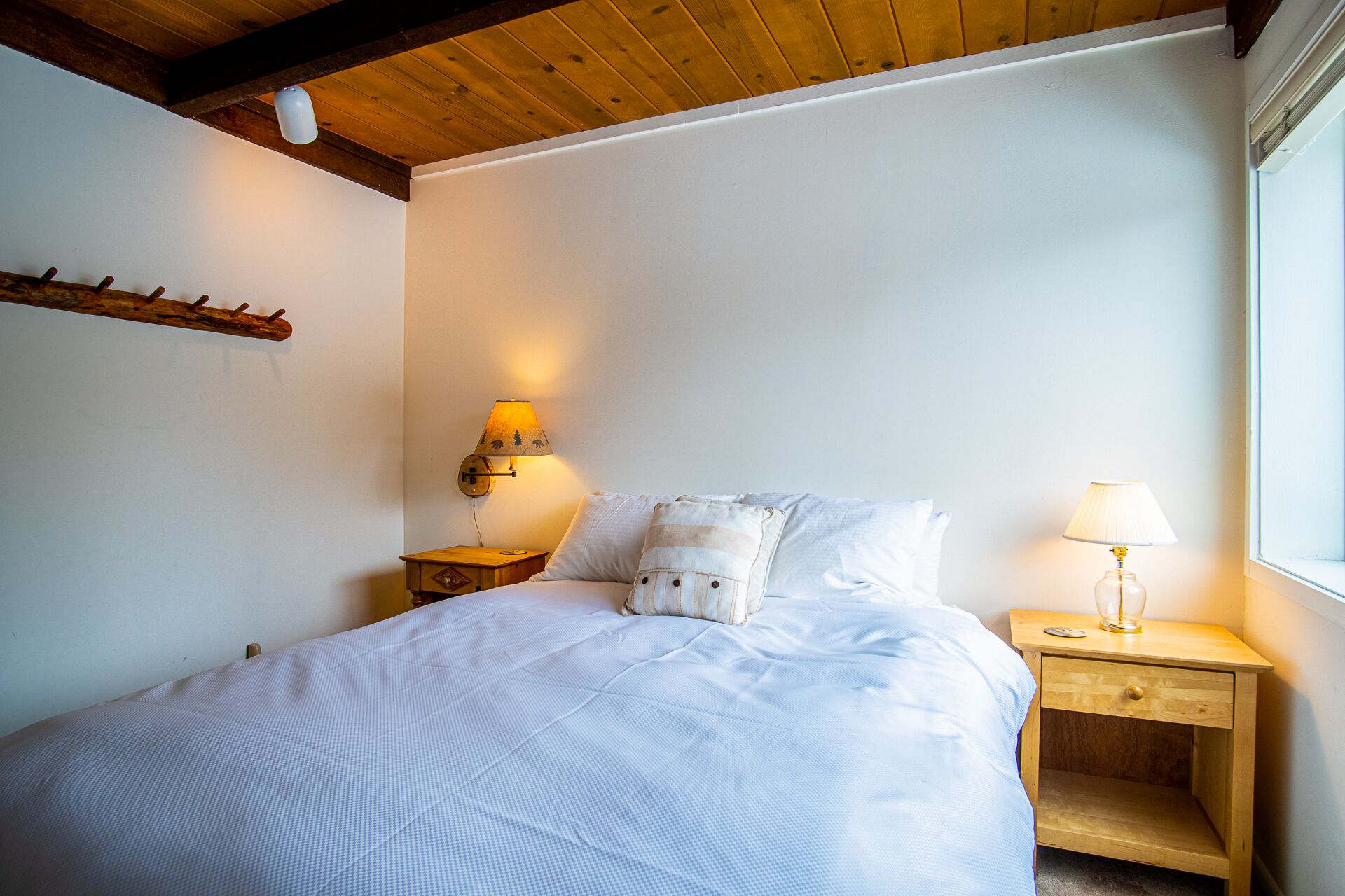 A bedroom with a bed, two bedside tables, a wall-mounted lamp, and a window.