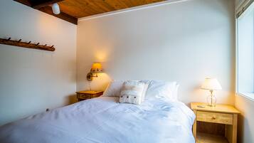 A bedroom with a bed, two bedside tables, a wall-mounted lamp, and a window.