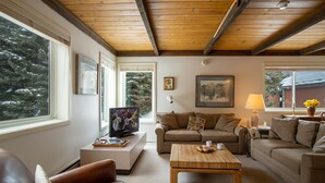 A cozy living room with a wooden ceiling, a television, a sofa, a coffee table, and a lamp.
