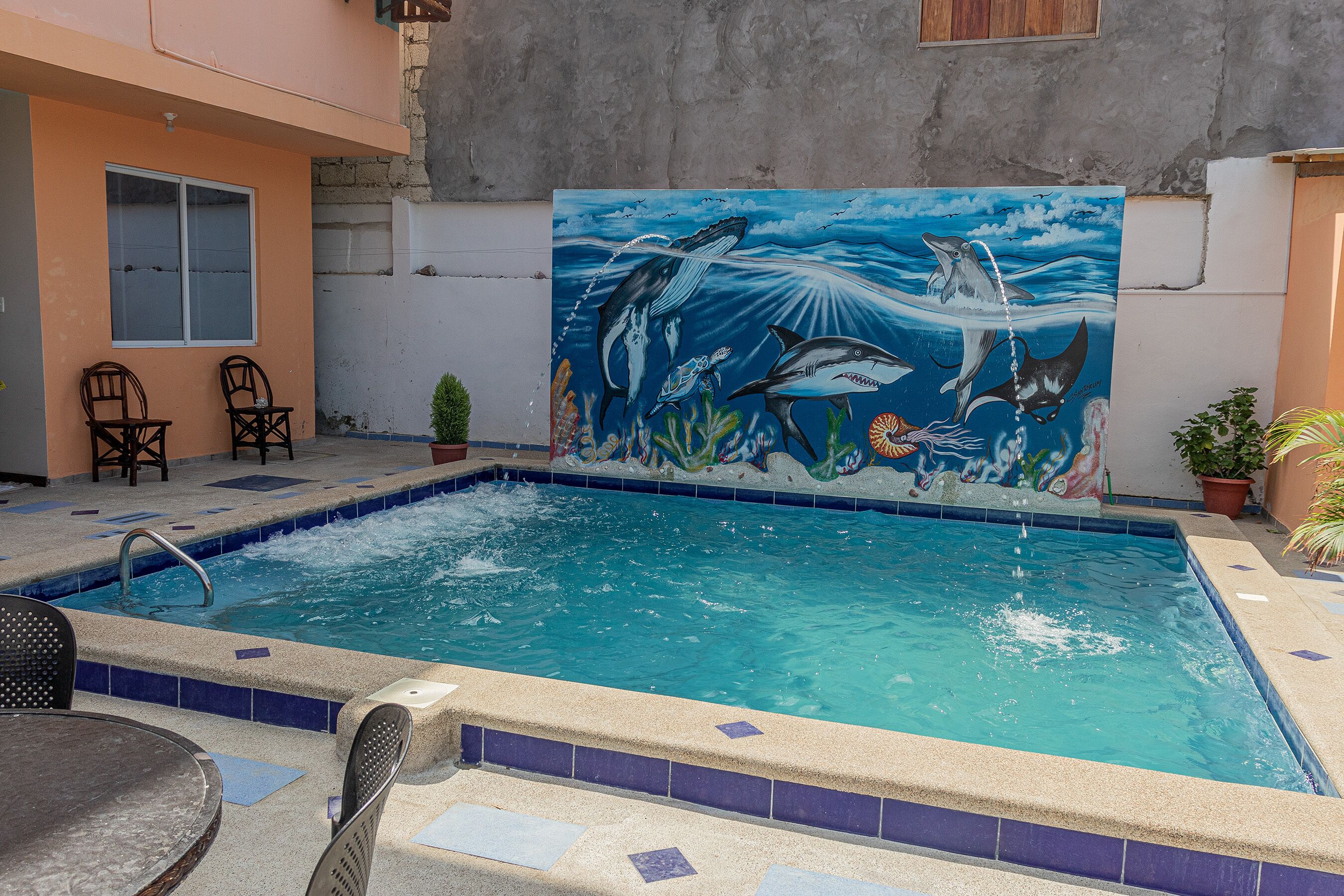 A swimming pool with a mural of marine life, surrounded by chairs and a small table.