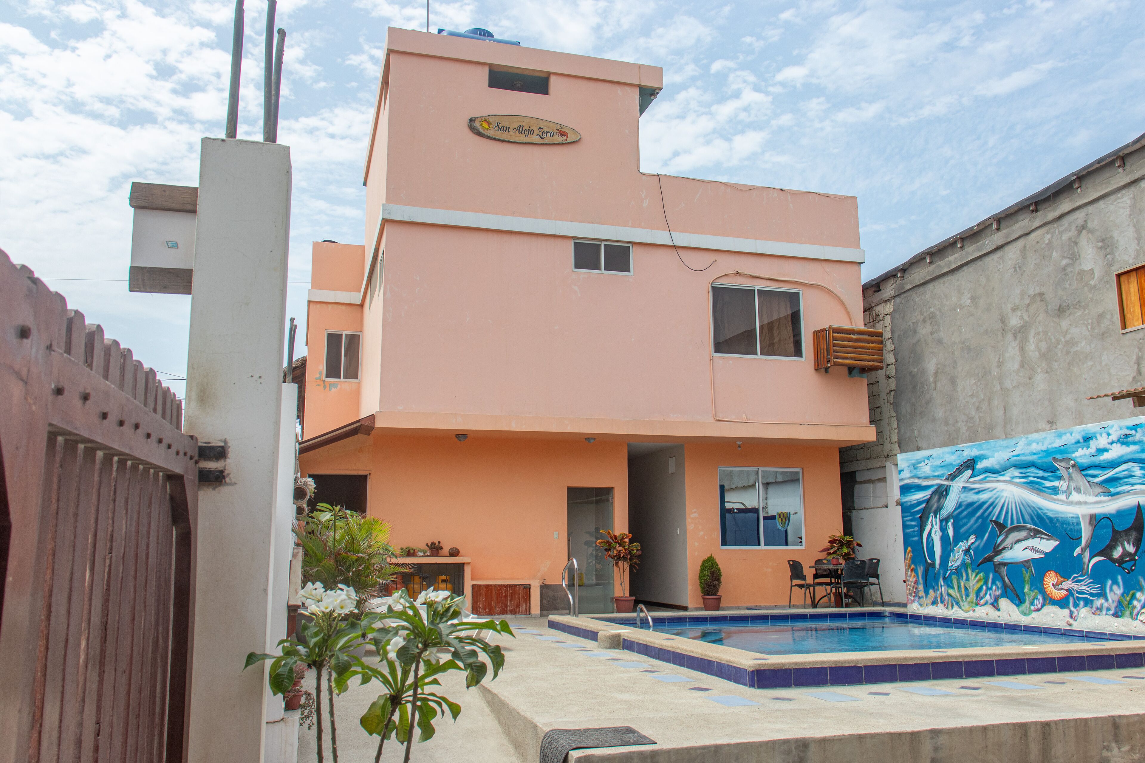 A two-story building with a swimming pool, a mural of marine life, and a sign that reads "San Alfonso Zero".