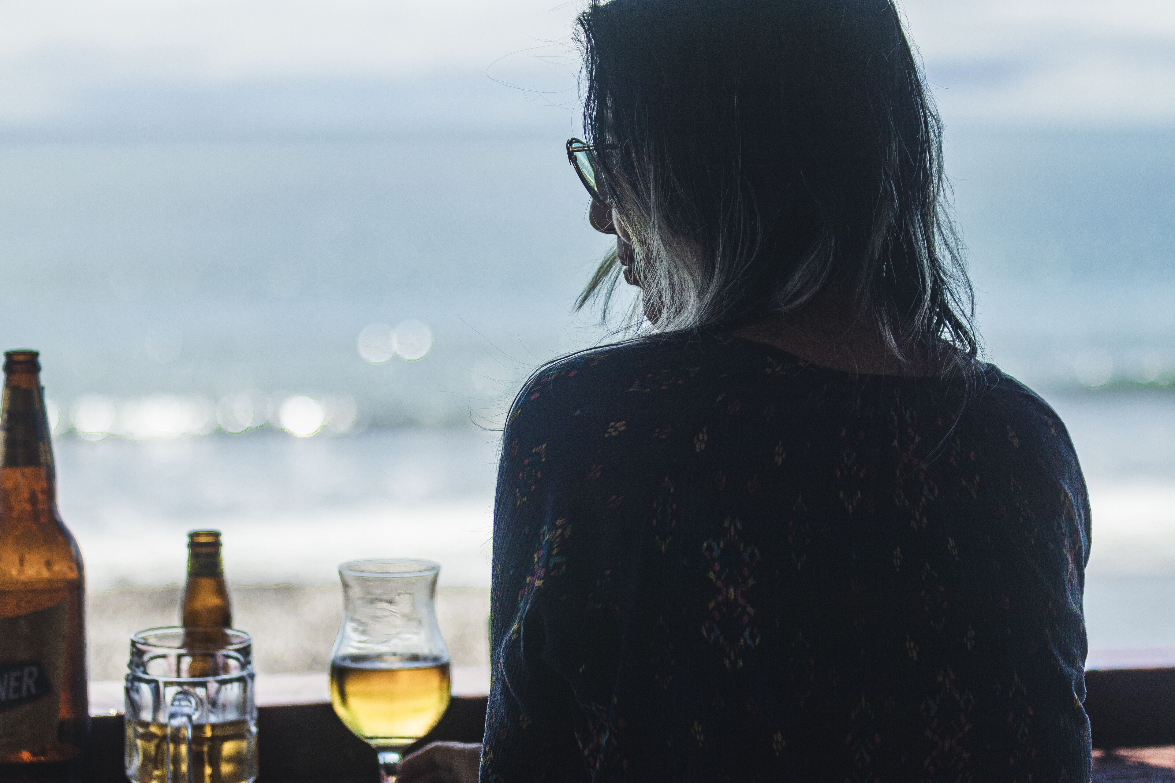 Una persona sentada a una mesa con una botella y vasos, con vista a un cuerpo de agua.