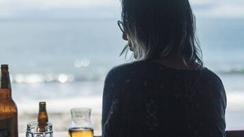 Una persona sentada a una mesa con una botella y vasos, con vista a un cuerpo de agua.