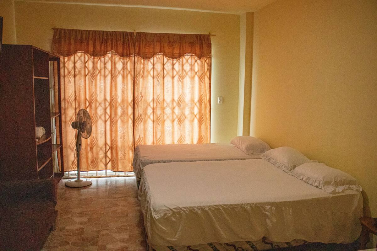 A room with two beds, a standing fan, and a wardrobe.