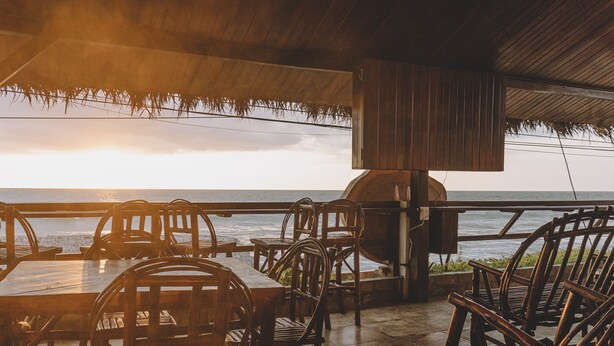 A wooden outdoor seating area with tables and chairs, overlooking the ocean. - San Alejo Zero (Charapoto)