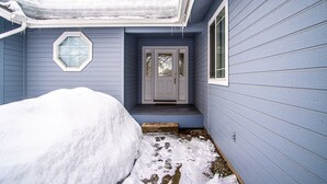 Un sentier étroit, recouvert de neige, mène à une maison dont la porte est grise et la fenêtre est ornée d’un vitrage dépoli.
