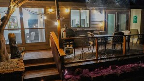 A cozy cabin with a wooden deck, a staircase leading to a lofted bedroom, and a dining area with chairs and a table. - 3 BR by Mabee Center ORU, Casino, Jenks, Victory Church (Tulsa)