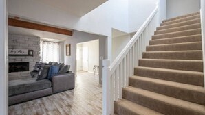 A living room with a grey sofa, a fireplace, and a staircase with beige carpet. - 3 BR by Mabee Center ORU, Casino, Jenks, Victory Church (Tulsa)