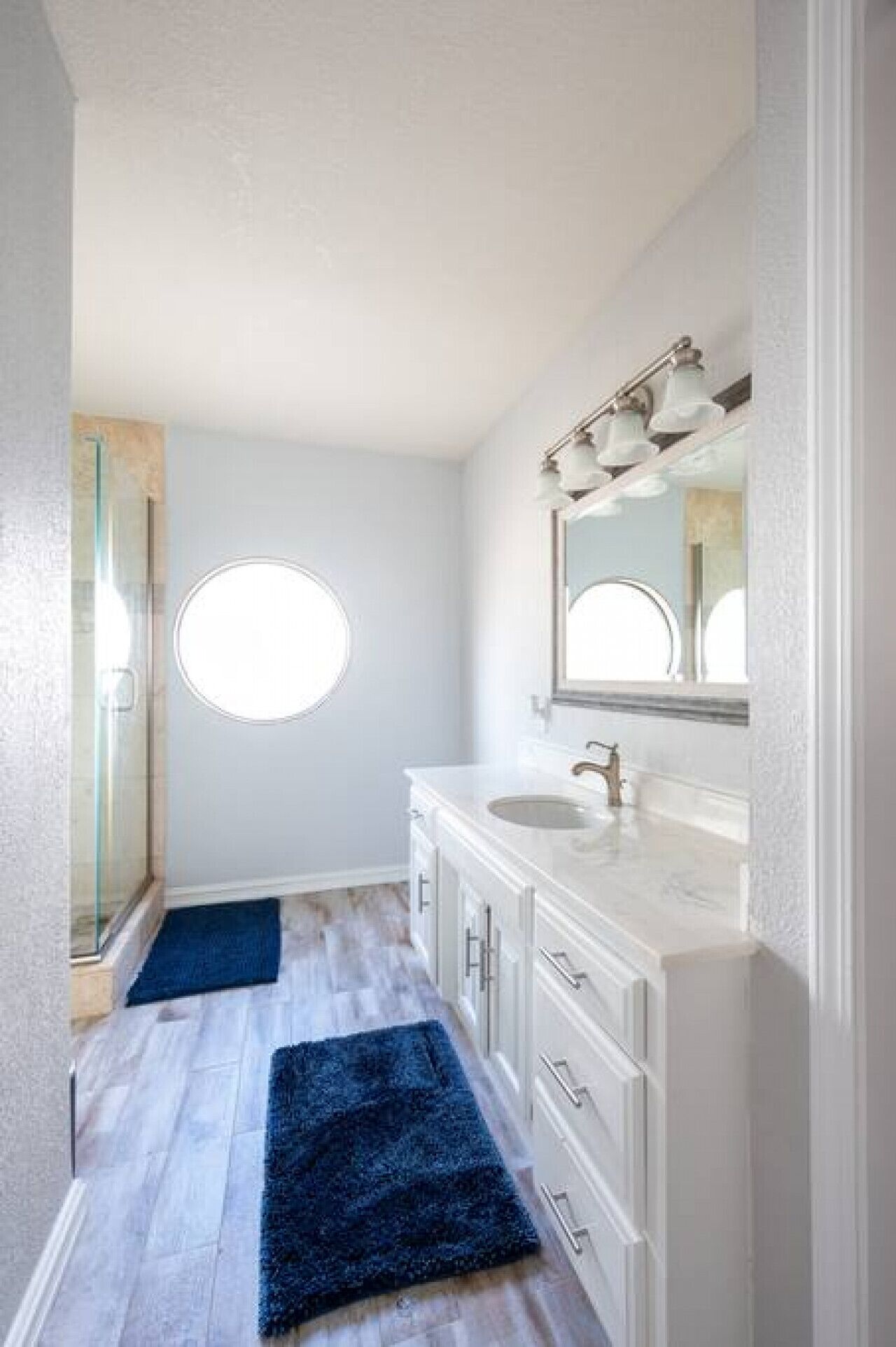 A bathroom with a white vanity, a round mirror, and a glass shower enclosure.