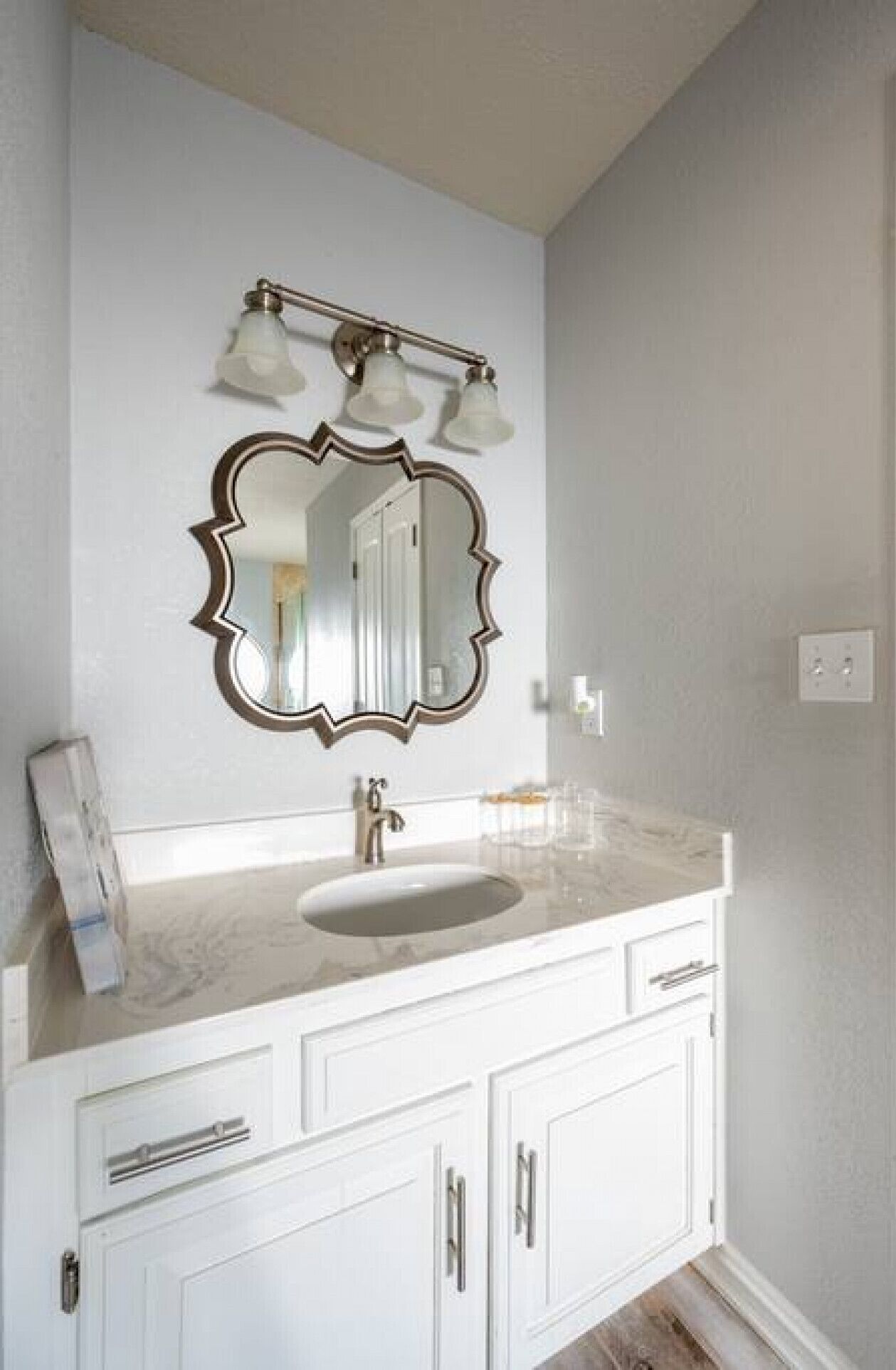 A bathroom with a white vanity, a large mirror with a decorative frame, and a light fixture above the mirror.