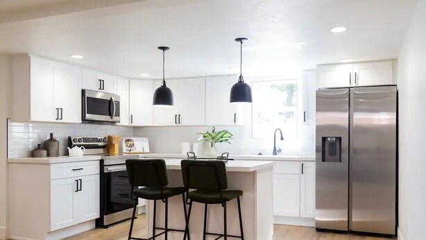 Een moderne keuken met witte kasten, roestvrijstalen apparatuur en zwarte hanglampen.