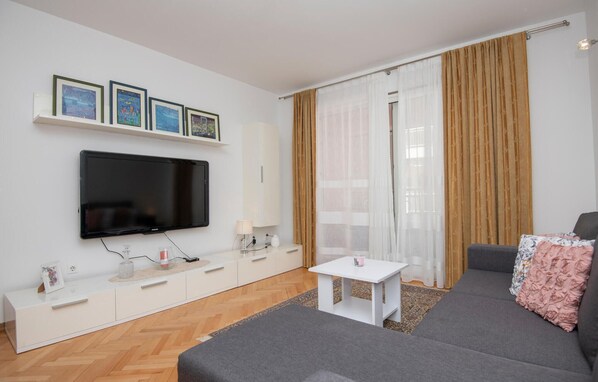 A modern living room with a flat-screen TV, a white console table, a grey sofa, and a small white table.