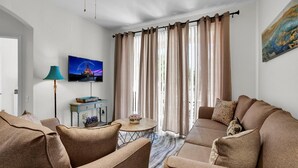 A living room with a sofa set, a television mounted on the wall, a lamp, and a window with curtains.