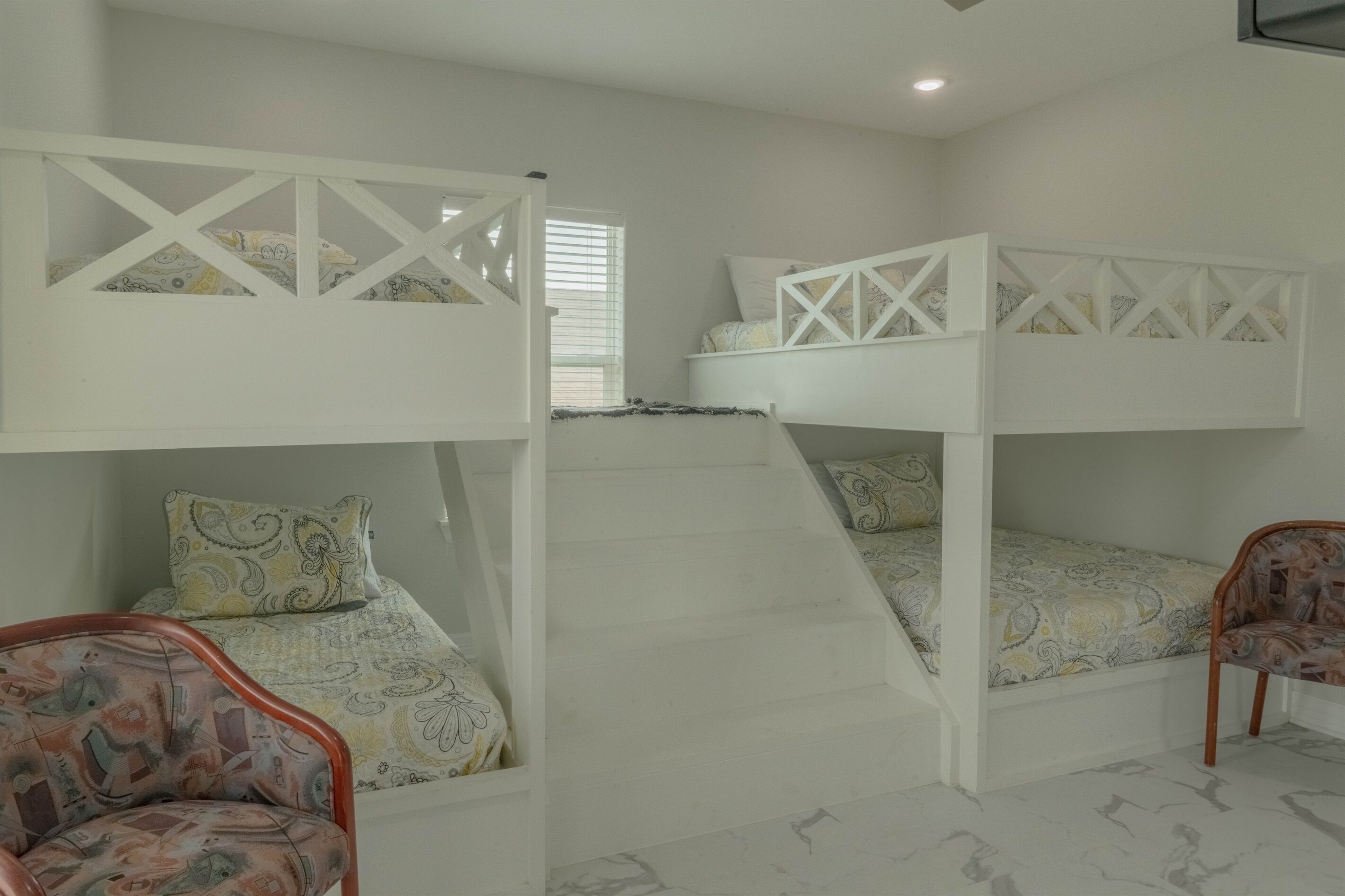 A room with bunk beds, a staircase, and patterned chairs.