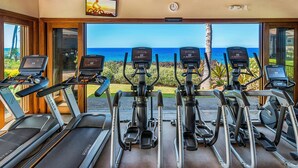 Un gimnasio con cintas de correr y máquinas elípticas, con vistas panorámicas al océano.