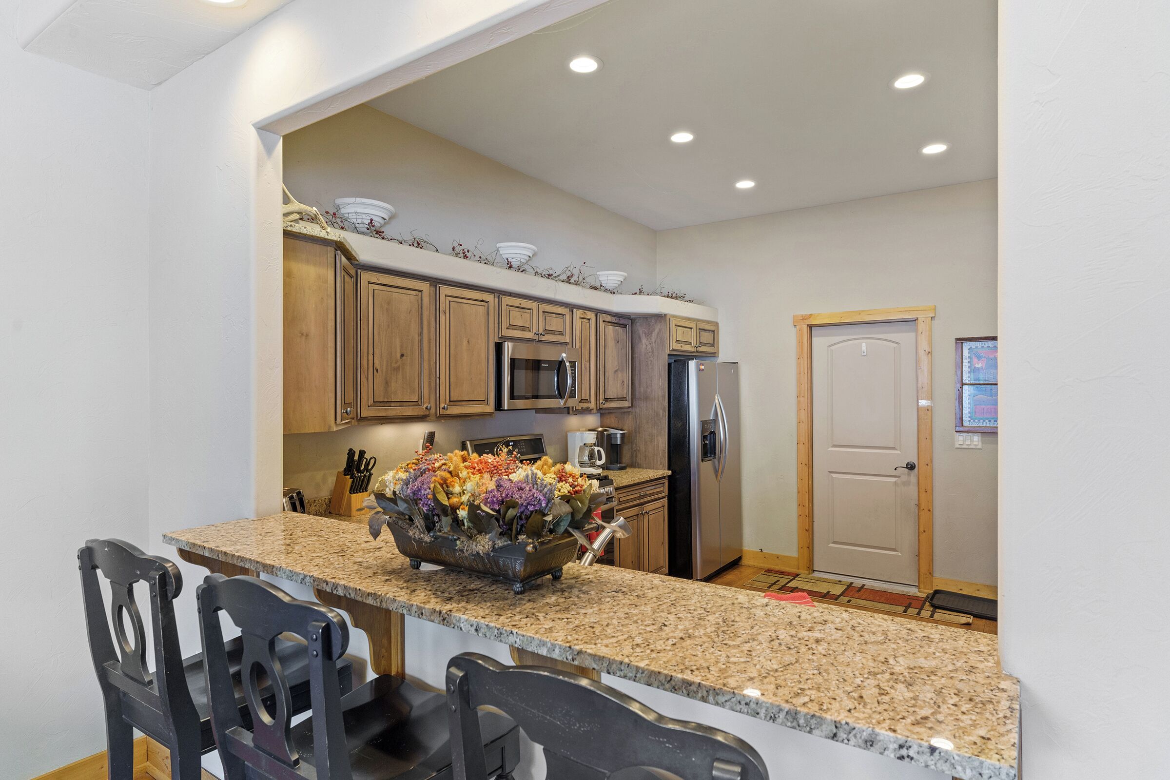A kitchen with granite countertops, wooden cabinets, stainless steel appliances, and a flower centerpiece.