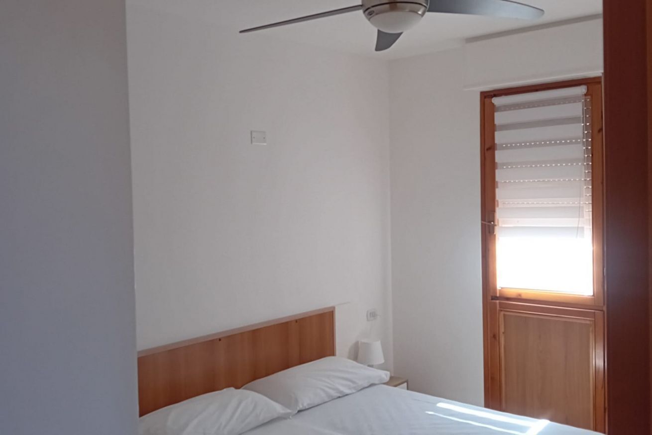 A bedroom with a wooden headboard, a ceiling fan, a window with blinds, and a door.
