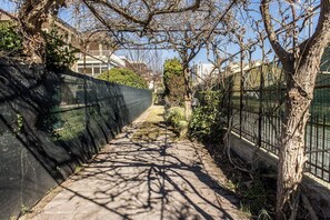 A narrow pathway flanked by trees and a fence, leading to a building in the distance.
